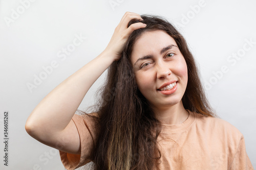 Dandruff and lice. Portrait of a young Caucasian brunette woman in a beige t-shirt, who strongly scratches her head with her hand. Copy space. White background