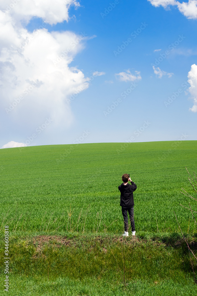 A young man in black clothes on a field of green young wheat shoots a picturesque landscape. Travel Ukraine.