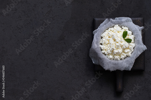 Cottage cheese on cheesecloth in a bowl on a wooden Board on a dark background top view photo