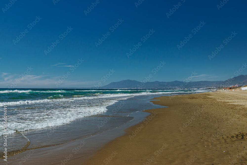 Fototapeta premium Empty beach in Marbella, Spain. Blue water, sandy beach, mountains.