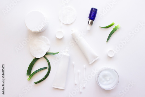 White squeeze tubes  bottles of cream  blue dropper glass serum with aloe vera  cotton pads and buds flat lay on white background top view copy space. Beauty skincare  natural cosmetic. Stock photo.