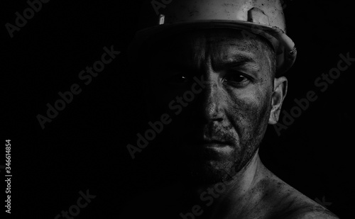Dirty coal miner in a yellow hard hat on a dark background in a black and white photo. photo