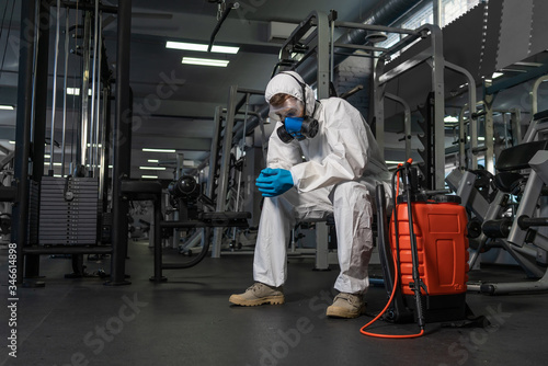 professional disinfector personal protective equipment ppe suit, gloves, mask, cleaning gym space with pressurized spray disinfectant water to remove covid-19 coronavirus photo