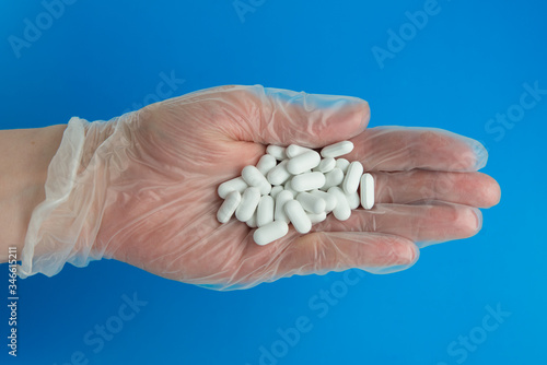 Doctor hand in medical glove holds lots of white pills.