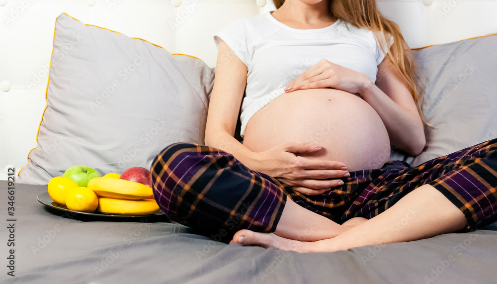 Healthy Nutrition During Pregnancy. Concept of expectation of the child, pregnancy and motherhood. Young pregnant woman sits at home in bed with plate of fresh fruit. Happy pregnancy, waiting for baby Healthy Nutrition During Pregnancy. Concept of expectation of the child, pregnancy and motherhood. Young pregnant woman sits at home in bed with plate of fresh fruit. Happy pregnancy, waiting for baby