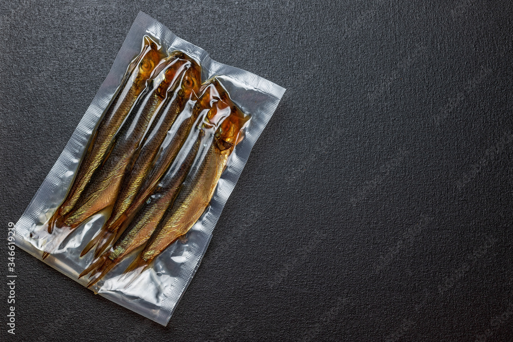 Smoked herring fish, in a vacuum transparent package, on a black background Smoked herring fish, in a vacuum transparent package, on a black background