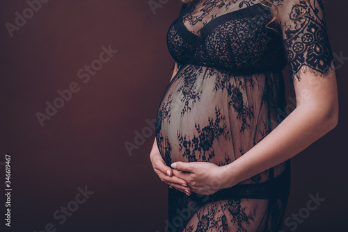 Pregnant woman belly in black lace on brown chocolate background