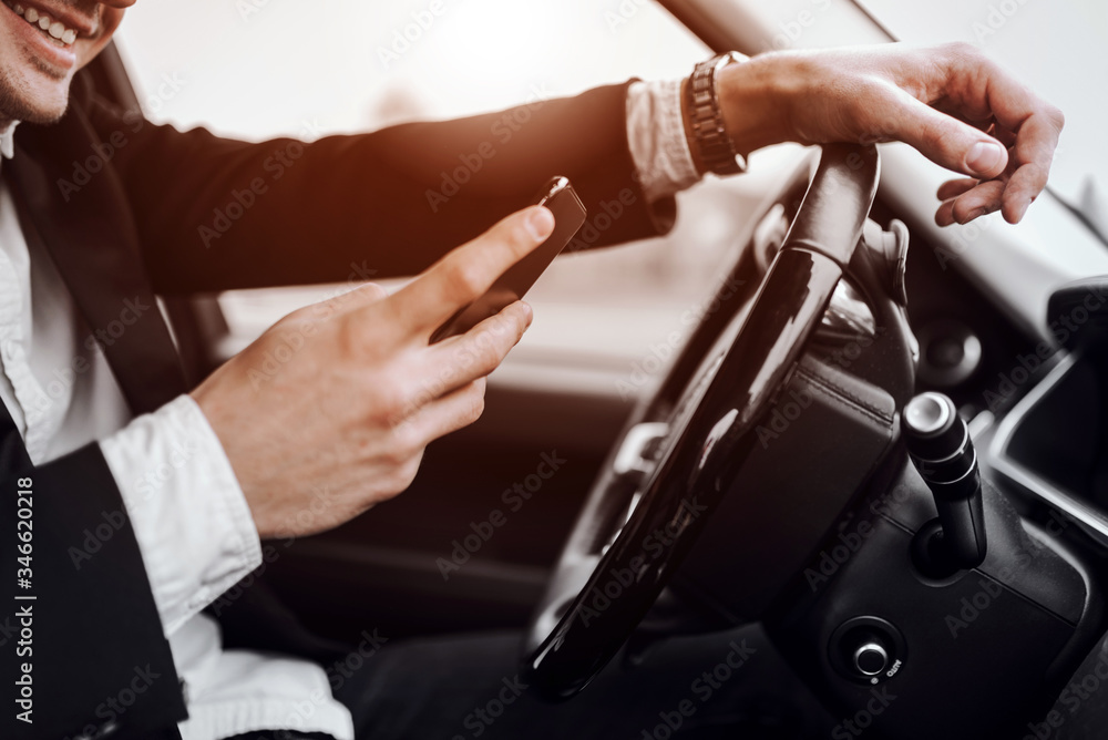 Naklejka premium Smiling young man is holding mobile phone in car
