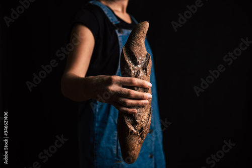 Fototapeta Naklejka Na Ścianę i Meble -  A woman hand holding a handmade rye bread from the bottom on a black background. Her hand is spotted with flour.