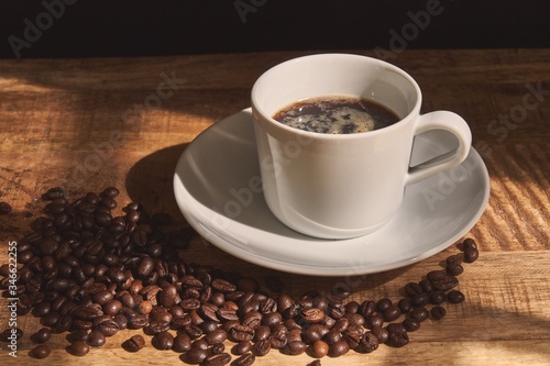 Close-up of cup of coffee with grains scattered next to it on wooden table.