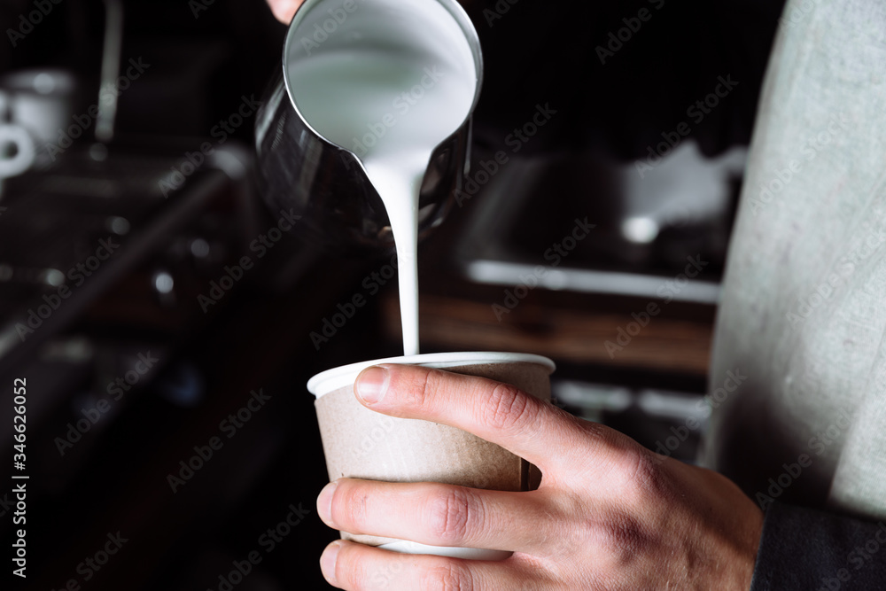 Barista pours warm milk into coffee.
