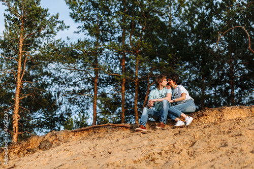 Lovers sit on a sandy cliff against the background of a forest