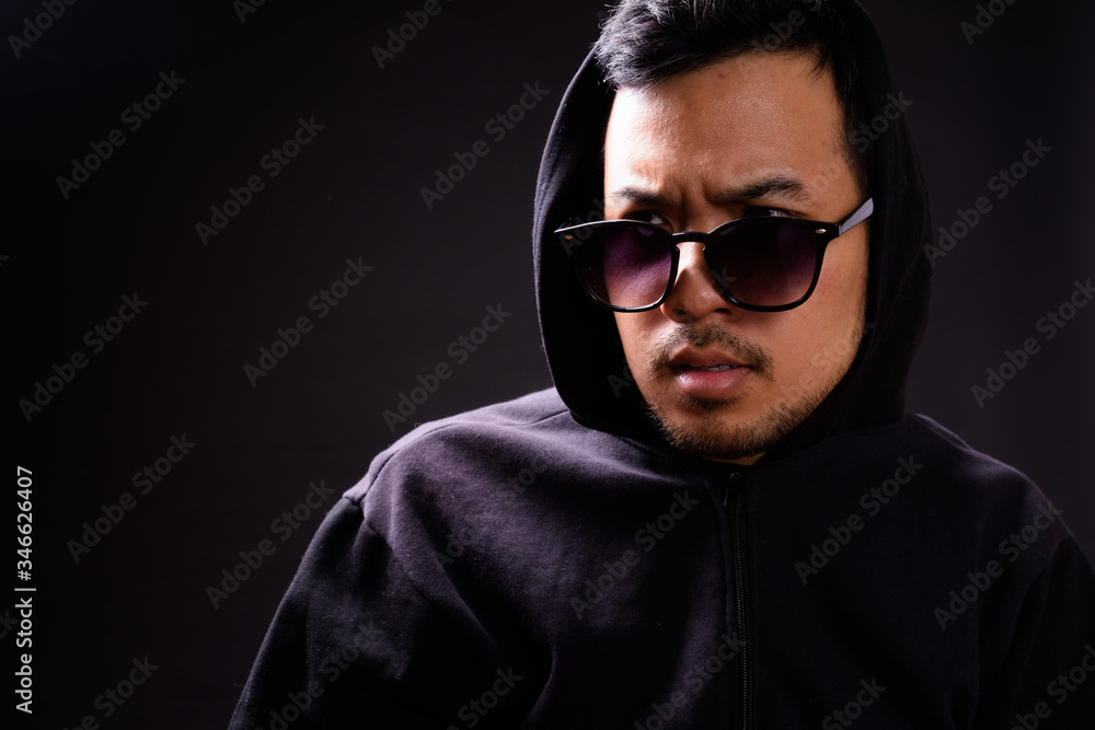 Portrait of young Asian man in hoodie peeking through sunglasses Portrait of young Asian man in hoodie peeking through sunglasses