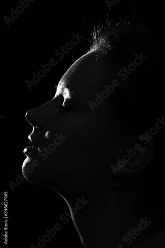 Profile of a woman. Silhouette  Black and white portrait of girl with long hair. Top light. Dramatic girl on a dark background.  Concept of hope,  prayers and religion. Woman with  closed eyes.