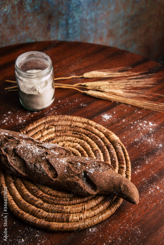 Handmade rye bread over a wooden table with spikes and a flour jar