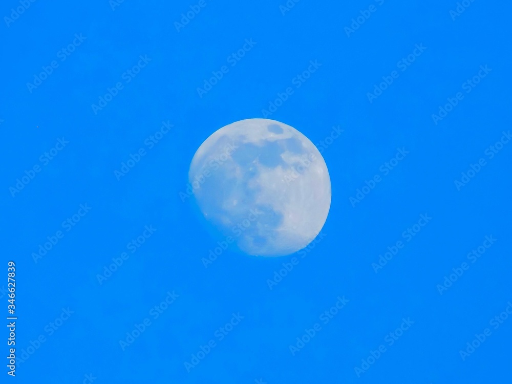 Big, almost full super moon cached on blue afternoon sky in cloudless February day Big, almost full super moon cached on blue afternoon sky in cloudless February day