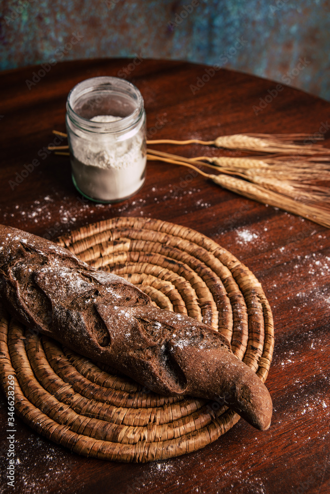 Handmade rye bread over a wooden table with spikes and a flour jar.