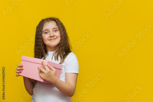 Little cute girl holding gift box on Yellow background.