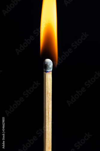Single matchstick on fire in front of black background.