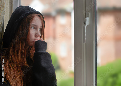 Depressed teen girl in warm wear standing near window