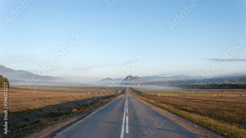The road goes to the horizon. On a mountain horizon with fog. Around the field with cows