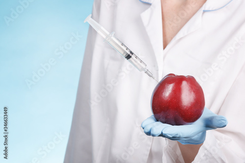a syringe is stuck in an Apple in the hand on a blue background. concept of genetically modified vegetables and fruits