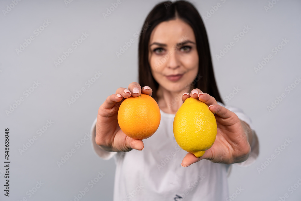 Cute girl in white t-shirt holds in two hands the orange and the lemon, she thinks what to choose Cute girl in white t-shirt holds in two hands the orange and the lemon, she thinks what to choose