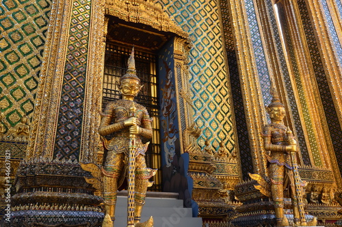 Golden guardian in front of a wall of mosaics at Wat Phra Kaew in Bangkok