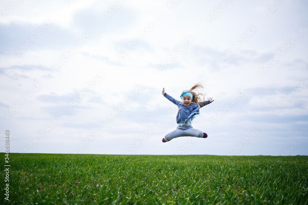 little girl child runs and jumps, green grass in the field, sunny spring weather, smile and joy of the child, blue sky with clouds