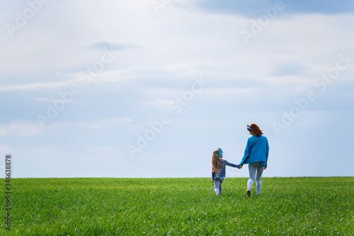 little girl child and mother woman run and jump, green grass in the field, sunny spring weather, smile and joy of the child, blue sky with clouds