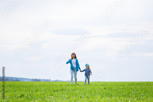little girl child and mother woman run and jump, green grass in the field, sunny spring weather, smile and joy of the child, blue sky with clouds © Дмитрий Ткачук