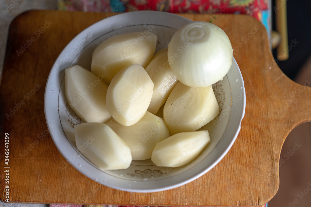 Raw peeled potatoes and peeled onions in a plate