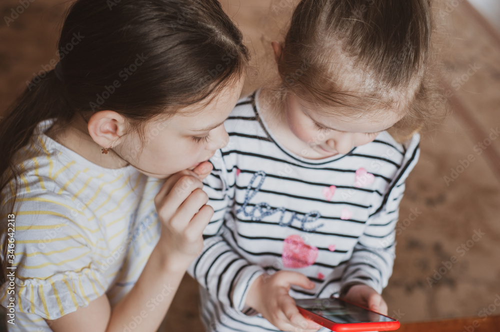 Happy little girls with a smartphone in hands communicate at home with loved ones using modern technology Happy little girls with a smartphone in hands communicate at home with loved ones using modern technology