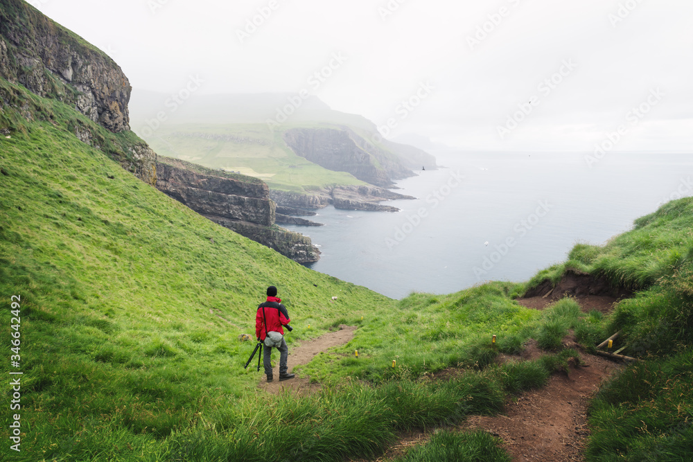 Foggy view of Mykines island with tourist in red jacket on the Faroe islands, Denmark. Landscape photography