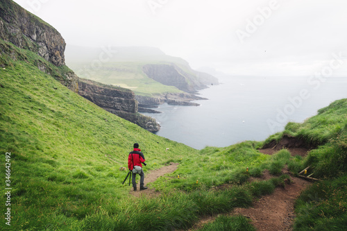 Foggy view of Mykines island with tourist in red jacket on the Faroe islands, Denmark. Landscape photography