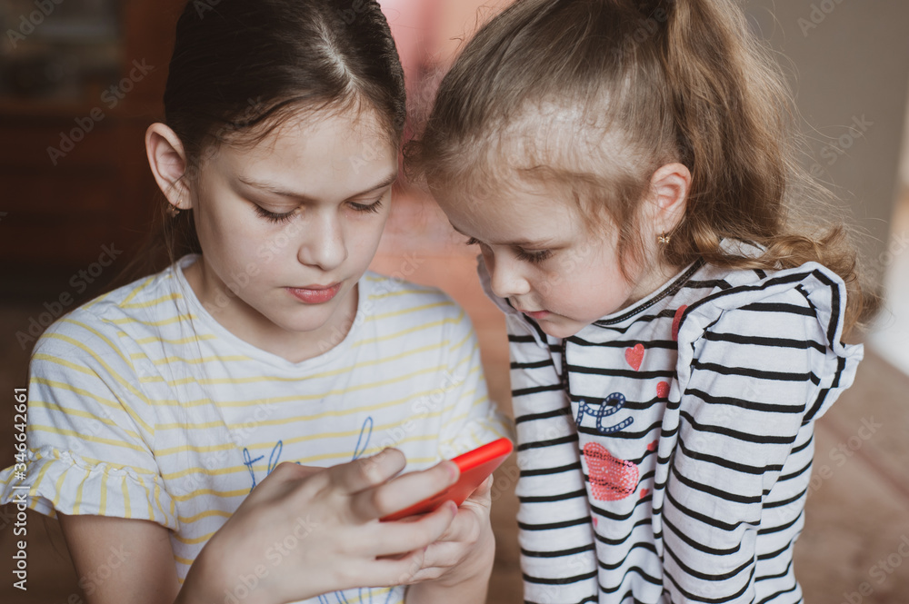 Happy little girls with a smartphone in hands communicate at home with loved ones using modern technology Happy little girls with a smartphone in hands communicate at home with loved ones using modern technology