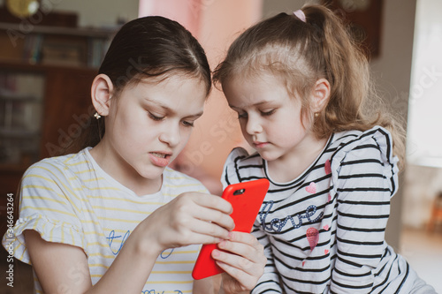 Happy little girls with a smartphone in hands communicate at home with loved ones using modern technology