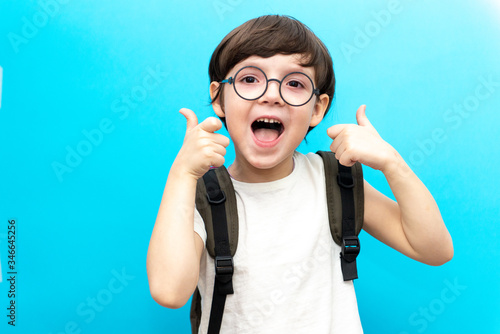 For the first time to school. Happy smiling boy with thumb up. A child from elementary school in uniform. Toddler indoors on a blue background. Funny baby