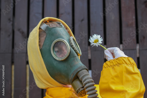 portrait of a human in a gas mask and in a yellow protective suit who holds a white flower in his hand