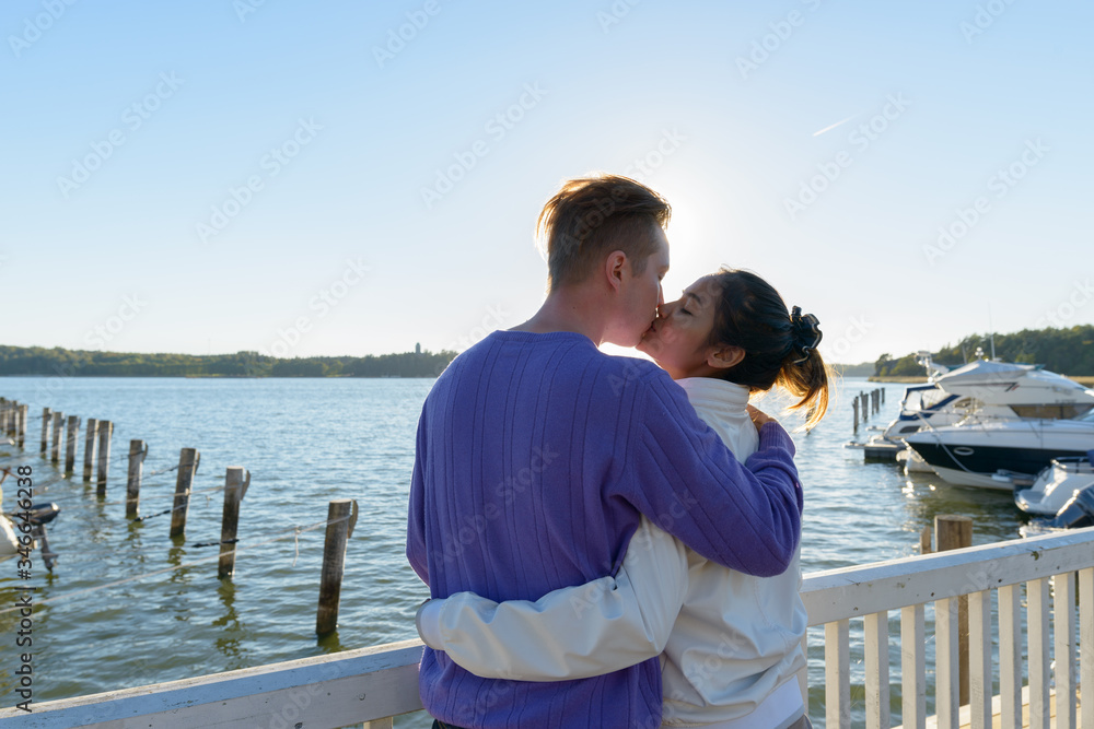 Rear view of young multi ethnic couple kissing each other at the pier outdoors Rear view of young multi ethnic couple kissing each other at the pier outdoors