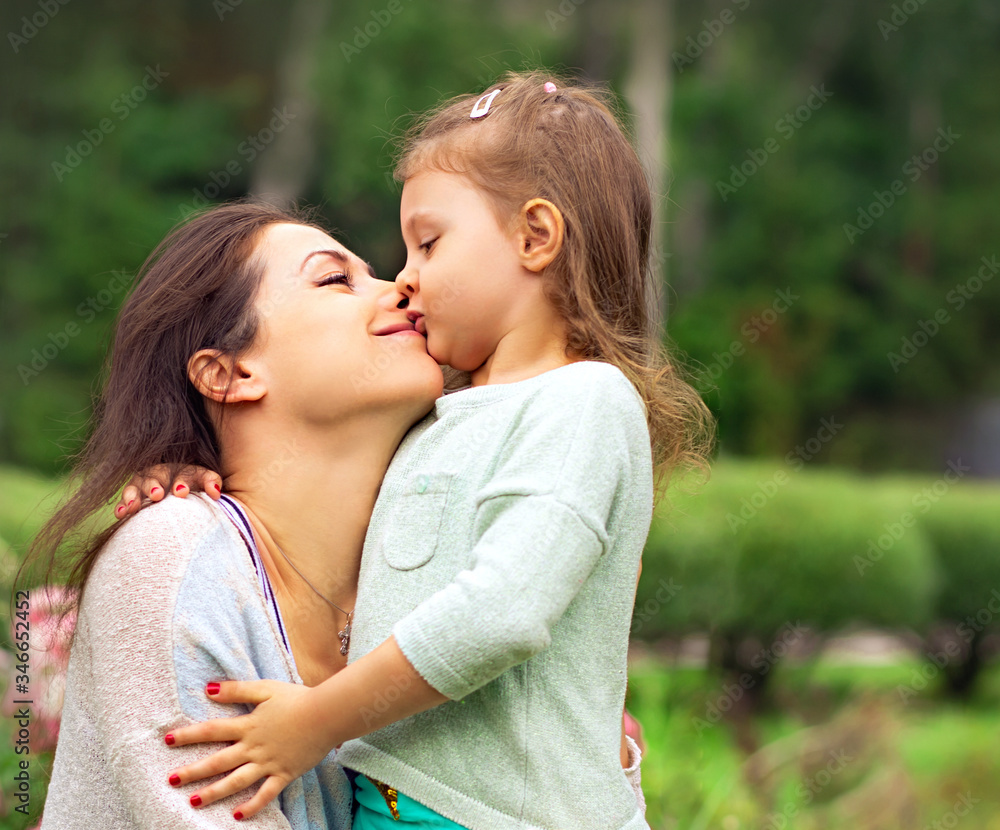 Beautiful mother and cute small daughter kissing on summer green background. Closeup Beautiful mother and cute small daughter kissing on summer green background. Closeup