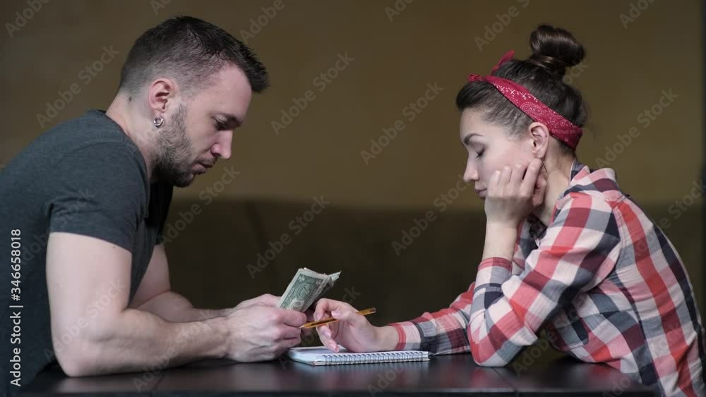 A man and a woman are sitting at the table and counting the rest of the money. A difficult period in a young family. A man and a woman are sitting at the table and counting the rest of the money. A difficult period in a young family.