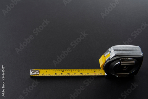 Flexometro o metro color plata con la cinta metrica amarilla sobre un fondo de color negro photo