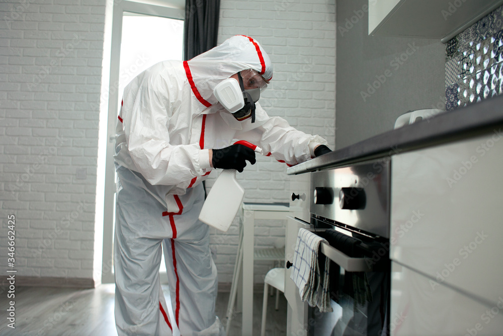 man in a protective suit and a respirator wipes furniture with a chemical agent, disinfects the room
