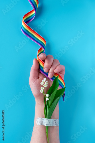 Thank you doctors and nurses! Rainbow ribbon in hand of mature woman with lily of the valley flowers. Bouquet attached with medical aid patch. Creative flat lay, top view on green background.