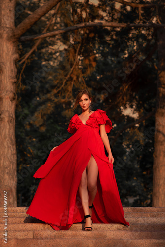 chic girl in a red long dress goes down the stairs, sunset