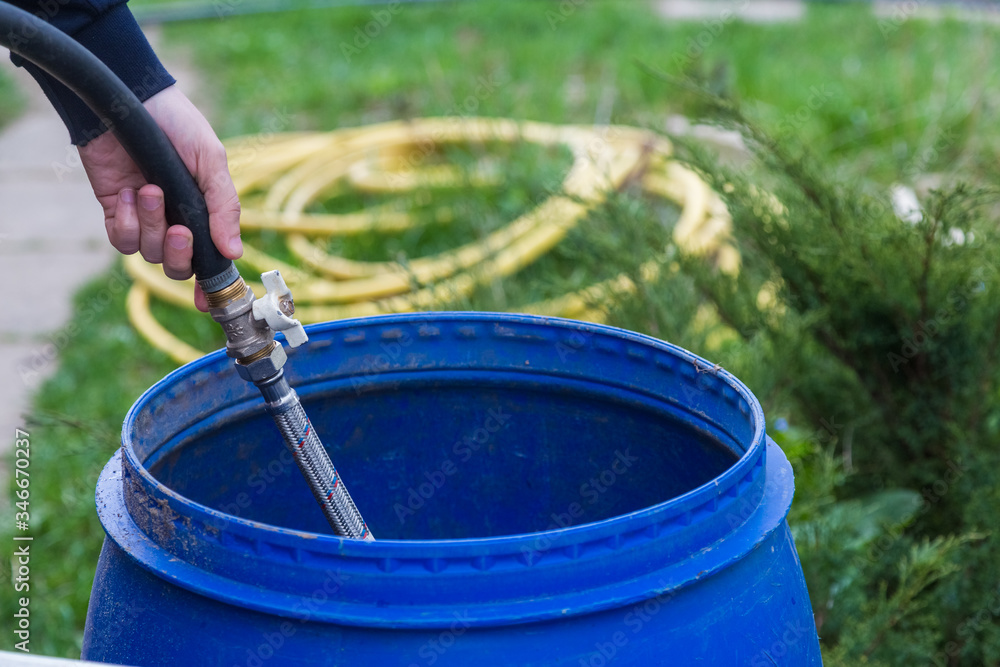 Cropped Hand Filling Water With Hose In Plastic Barrels Cropped Hand Filling Water With Hose In Plastic Barrels