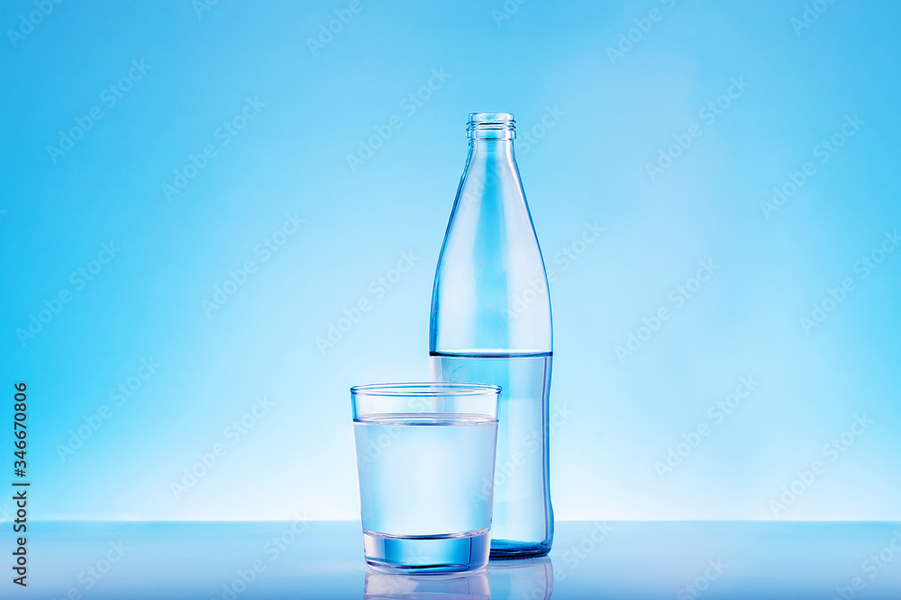 Clear mineral water bottle and glass on blue background with copy space. Clear mineral water bottle and glass on blue background with copy space.