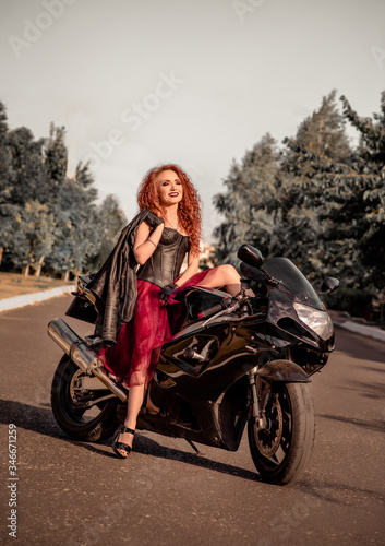 girl with red hair in black corset and red skirt on a black motorcycle