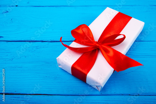 Box in Kraft paper, ECO-paper on a wooden table. View from the top. A white paper-wrapped gift box with a red satin ribbon bow on an old rustic blue wood background. For your design. Flat lay